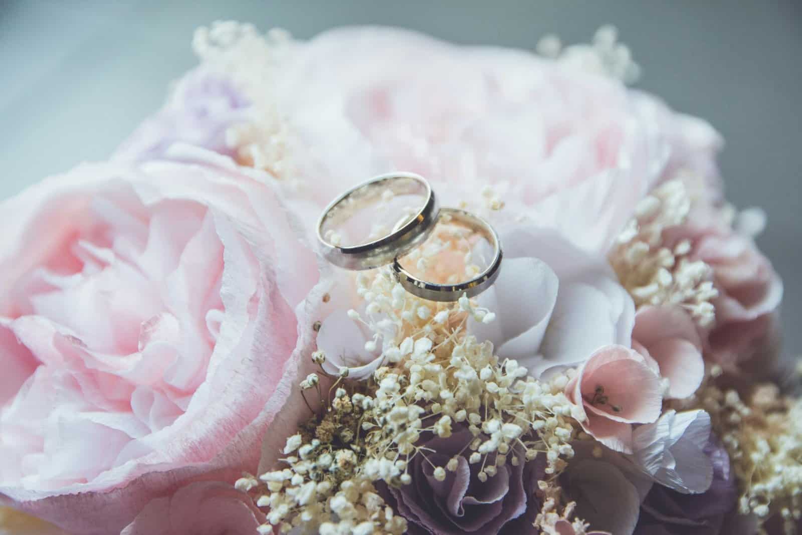 Elegant wedding rings on a soft pink flower arrangement, symbolizing love and commitment.