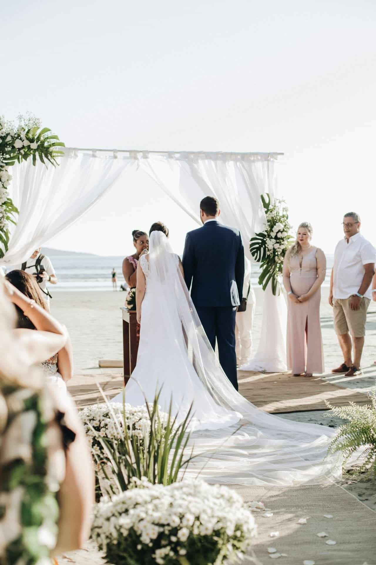 Beautiful beach wedding ceremony with bride and groom under a white canopy.