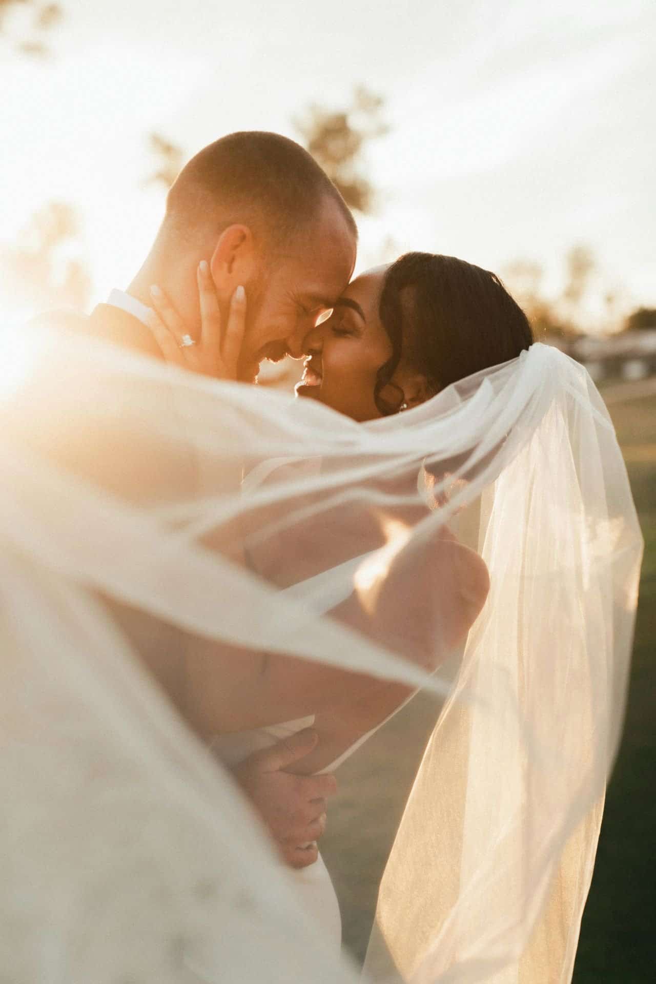 Romantic couple embracing outdoors with veil at sunset, wedding scene.
