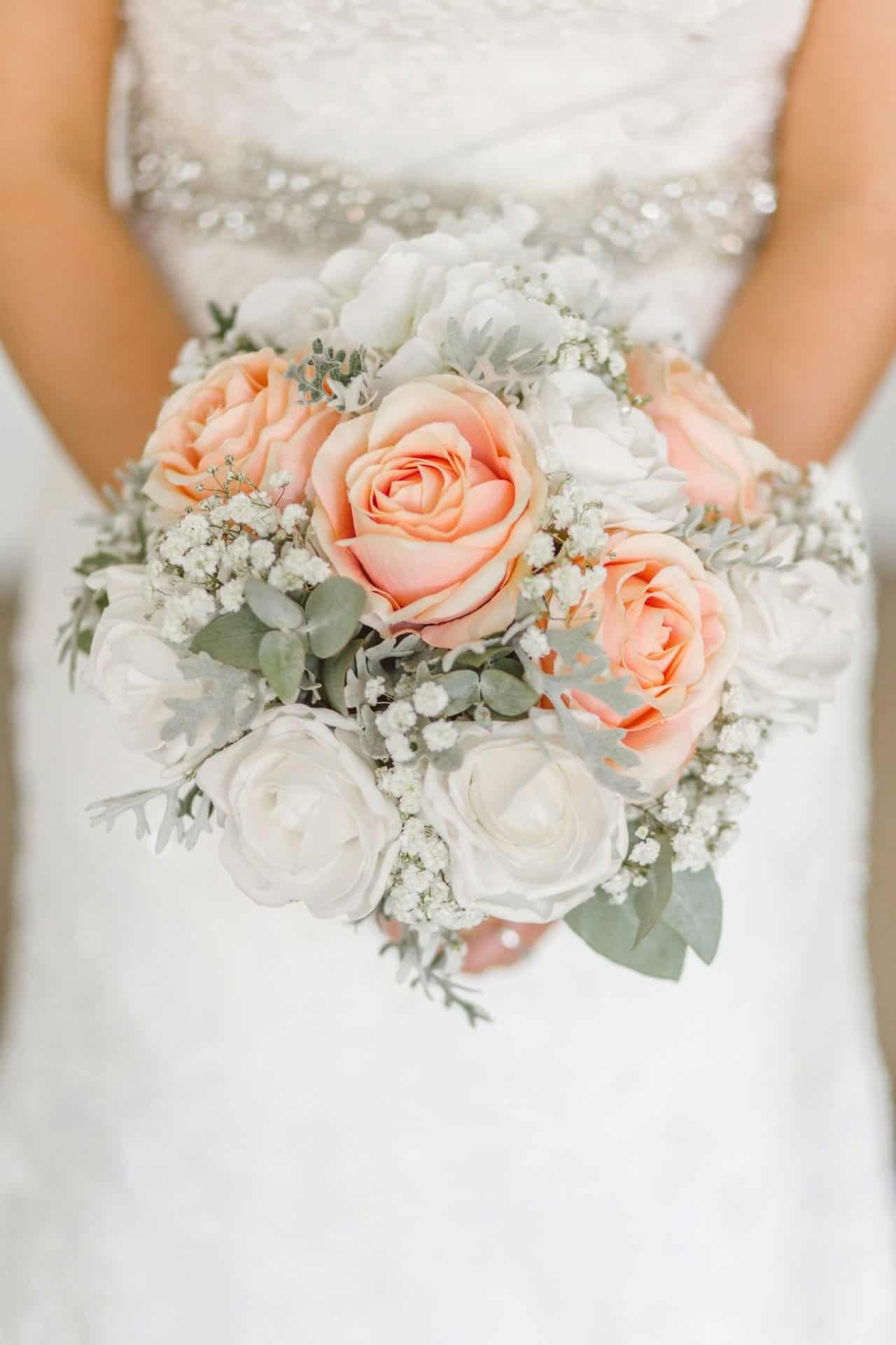 A lush bridal bouquet featuring peach roses, white ranunculus, and delicate baby's breath.
